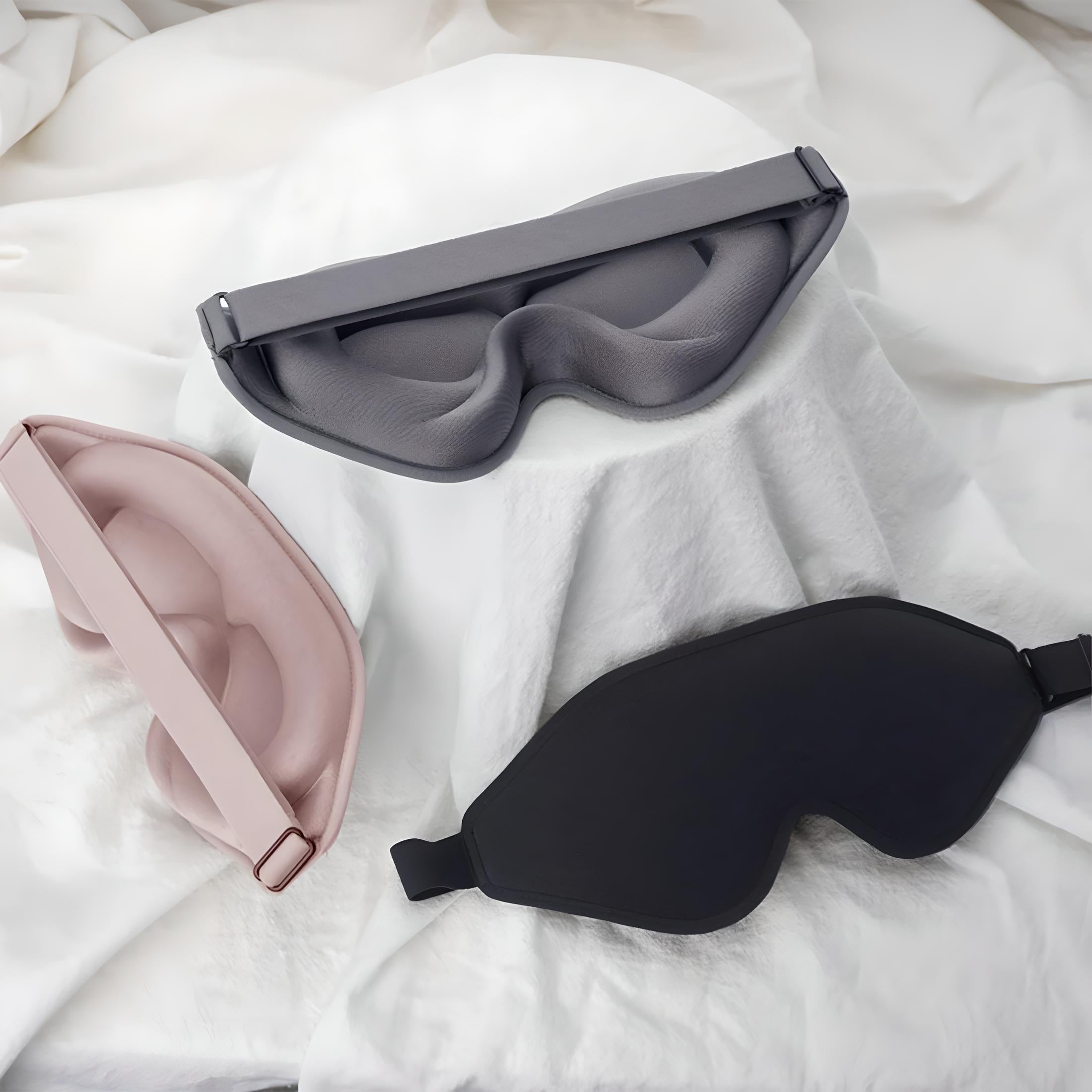Drei Schlafmasken aus Stoff in Schwarz, Grau und Rosa auf weißem Hintergrund.