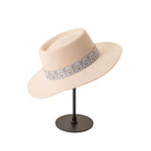 Beiger Filzhut mit breiter Krempe und gemustertem Band, elegantes Accessoire auf schwarzem Ständer.