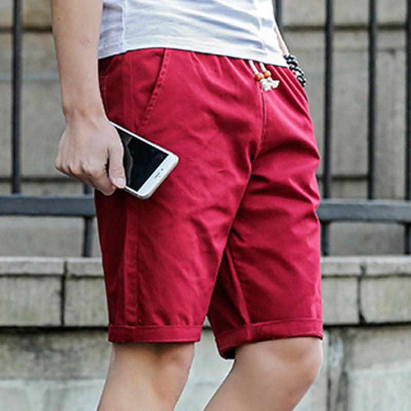 Mann in roten Baumwollshorts hält Smartphone, Sommermode, lässige Herrenbekleidung.