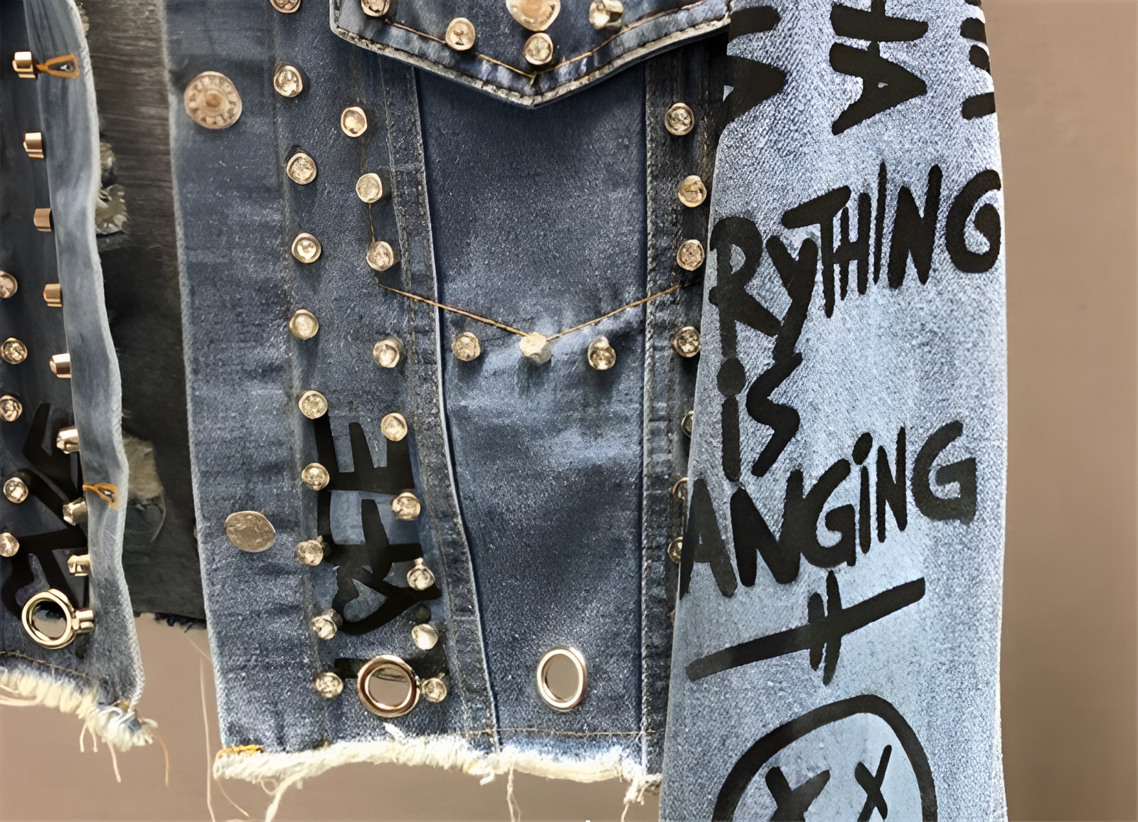 Jeansjacke mit Nieten und Graffiti-Design, verziert mit Schriftzügen und Fransen. Trendige Mode, Streetwear, Denim, urbaner Stil.
