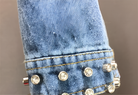 Nahaufnahme eines blauen Jeansstoffs mit Nieten und Strasssteinen. Modetrend, Denim, Verzierungen, Detailansicht, Textil, Bekleidung.