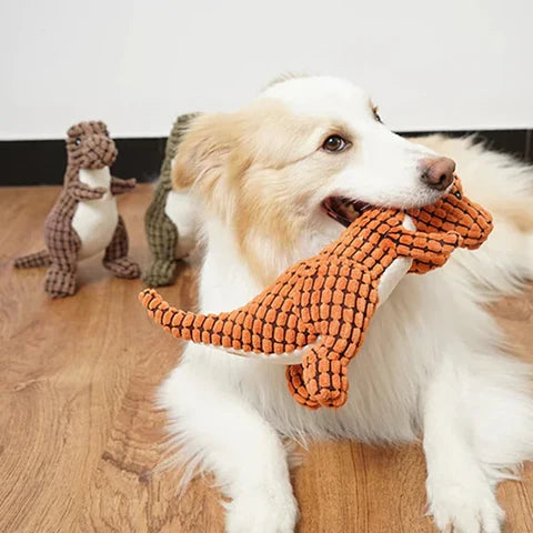 Hund spielt mit orangefarbenem Dinosaurier-Plüschtier, ideal für Haustierbedarf. Perfektes Hundespielzeug für interaktives Spielen und Zahnpflege.
