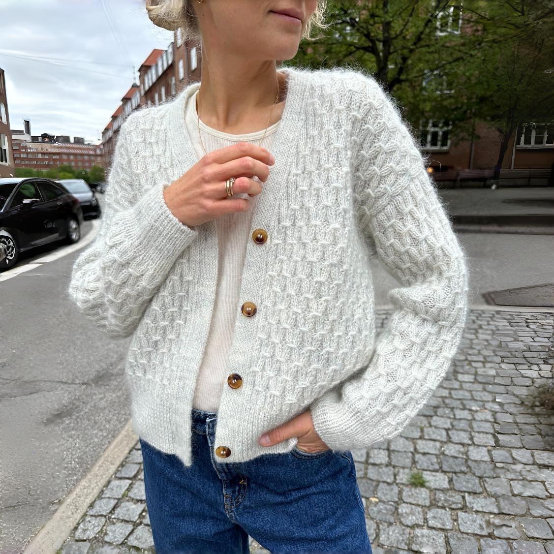 Frau trägt weißen Strickcardigan mit Holzknöpfen, kombiniert mit blauer Jeans. Modetrend, Herbstmode, Damenbekleidung, urbaner Stil.