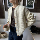 Frau trägt cremefarbene Strickjacke mit Knöpfen, hält Tasse. Modischer Herbst-Look, gemütlicher Strick, lässiger Stil, Damenmode.