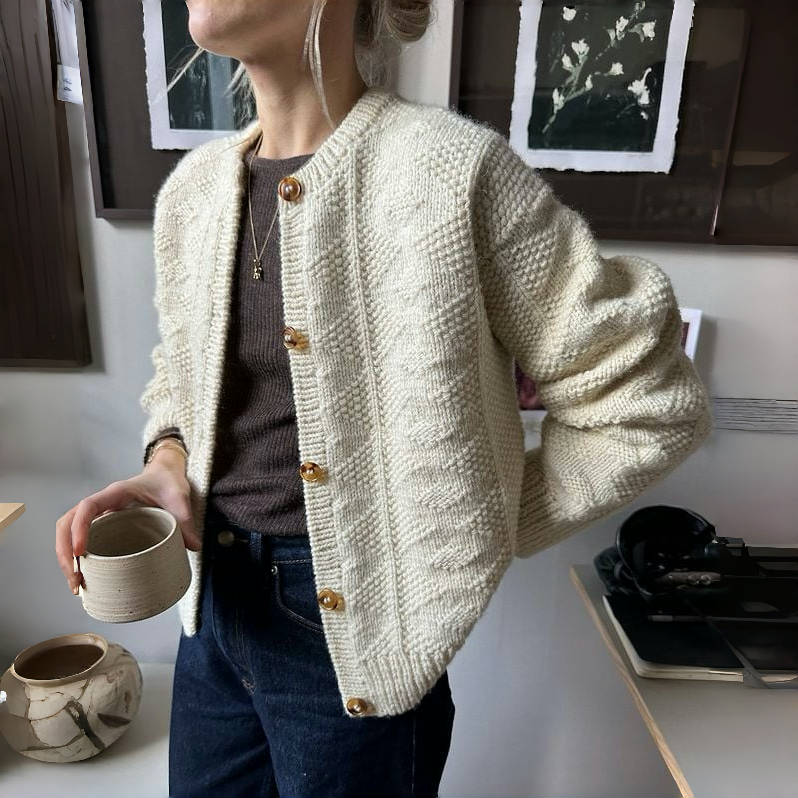 Frau trägt cremefarbene Strickjacke mit Knöpfen, hält Tasse. Modischer Herbst-Look, gemütlicher Strick, lässiger Stil, Damenmode.