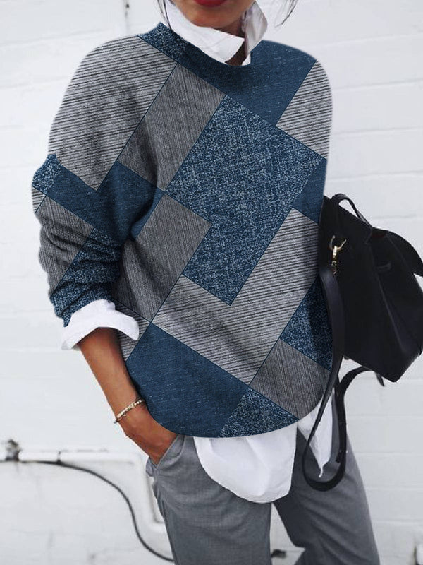 Damenpullover mit blau-grauem Patchwork-Design, lässig und modern. Perfekt für Herbstmode, kombiniert mit weißer Bluse und grauer Hose.