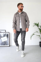 Mann in grauem Hemd und Jeans, trägt Sonnenbrille und weiße Sneaker. Moderne Herrenmode, lässiger Stil, urbaner Look, trendige Outfits.