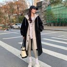 Frau in modischem Wintermantel, graue Leggings, weiße Sneakers, schwarze Kappe, trägt schwarze Tasche. Streetstyle, urbaner Look, Herbstmode.