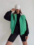 Damenmode: Grünes, ärmelloses Steppweste mit Reißverschluss, kombiniert mit schwarzem Hoodie und Radlerhose. Trendige Freizeitkleidung.