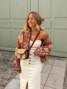 Frau in weißem Kleid mit Vintage-Patchwork-Jacke und Umhängetasche. Herbstmode, lässig, stilvoll, Damenbekleidung, trendige Outfits.