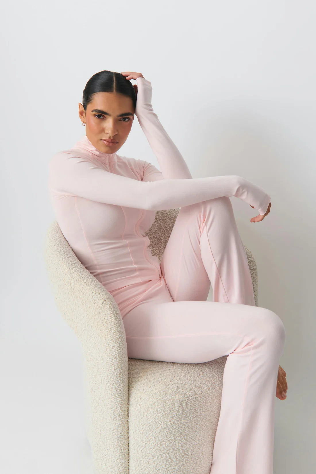 Frau in rosa Ganzkörperanzug sitzt auf modernem Sessel. Modetrend, elegantes Design, bequeme Damenmode, stilvolle Freizeitkleidung.