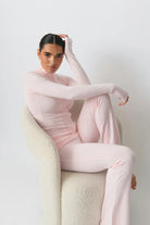 Frau in rosa Ganzkörperanzug sitzt auf modernem Sessel. Modetrend, elegantes Design, bequeme Damenmode, stilvolle Freizeitkleidung.