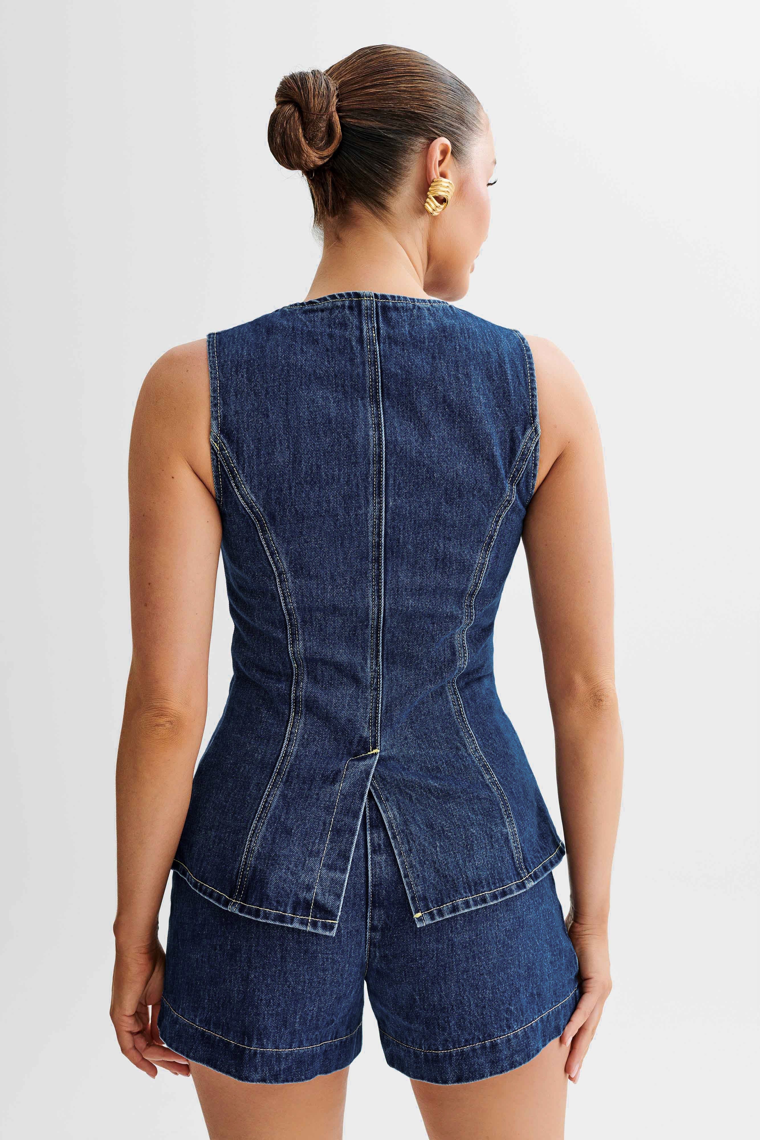 Frau in ärmellosem, tailliertem Jeans-Top und Shorts, Rückansicht. Modetrend, Denim-Outfit, Sommermode, lässiger Stil, Damenbekleidung.
