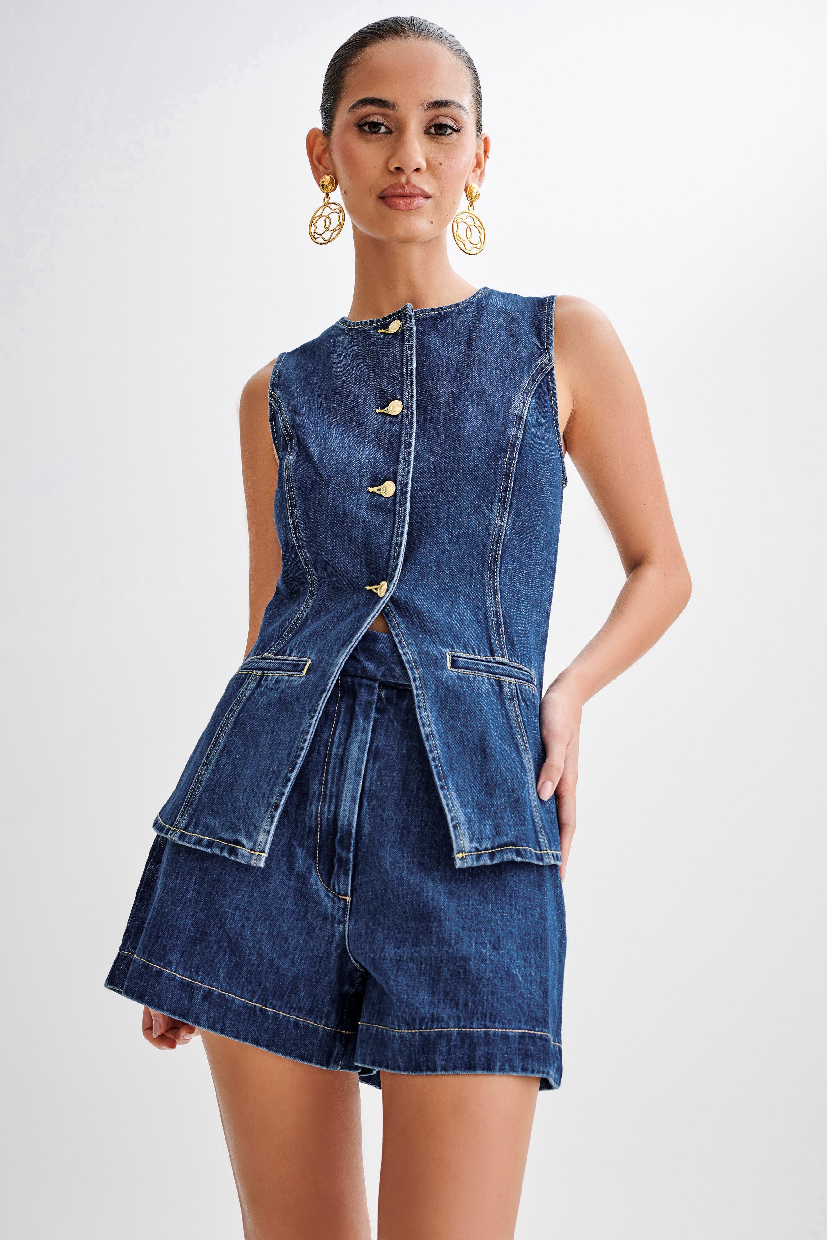 Frau in ärmelloser Jeansjacke und Shorts, goldene Ohrringe, modisch, elegant, Denim-Look, Sommermode, trendige Damenbekleidung.