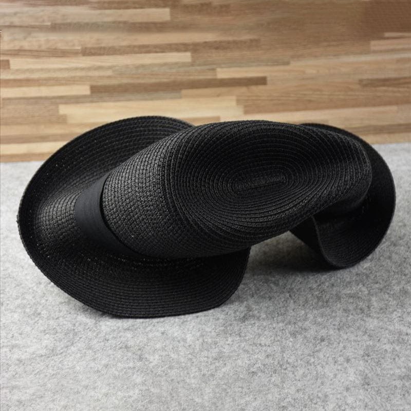 Schwarzer, geflochtener Strohhut, flexibel, auf grauem Hintergrund, modisches Accessoire.