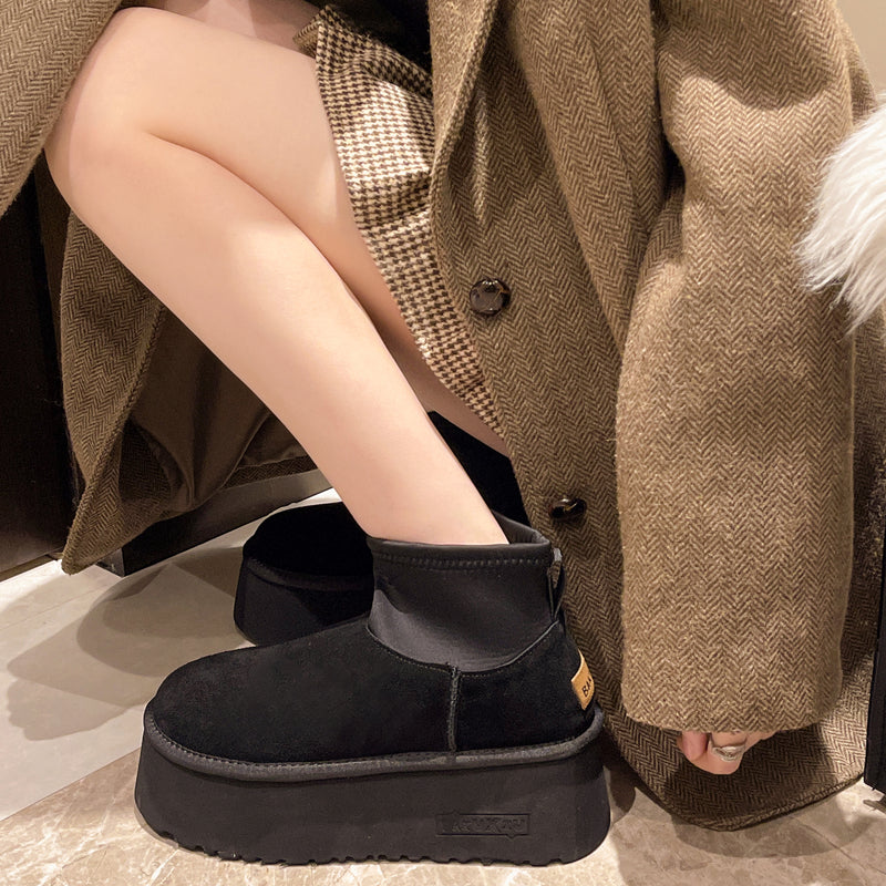 Damenstiefel mit Plateau, schwarz, aus Wildleder, kombiniert mit kariertem Rock und braunem Mantel. Modische Herbst-/Winterkleidung.