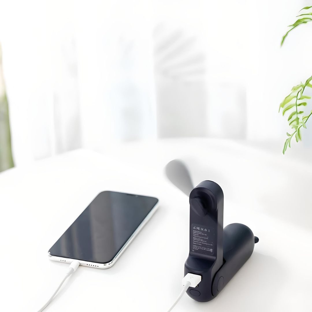 Schwarzer tragbarer Mini-Ventilator mit USB-Anschluss neben Smartphone auf weißem Tisch.