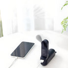 Schwarzer tragbarer Mini-Ventilator mit USB-Anschluss neben Smartphone auf weißem Tisch.