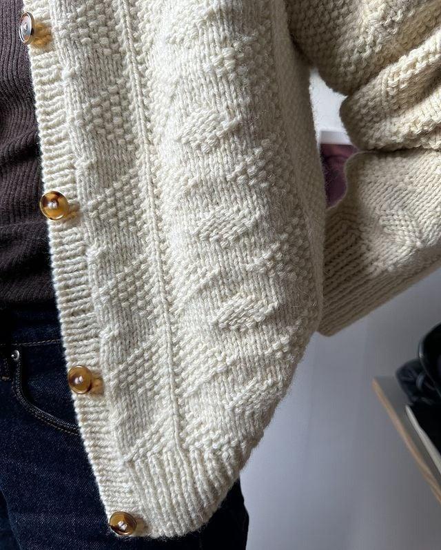 Beige Strickjacke mit Zopfmuster und Holzknöpfen, kombiniert mit dunkler Jeans. Modetrend, Herbstmode, Strickmode, Damenbekleidung.