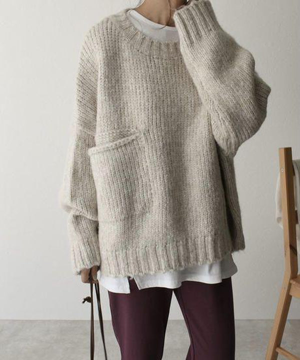 Beiger Oversize-Pullover aus grobem Strick mit Rundhalsausschnitt und großer Tasche, ideal für gemütliche Herbst- und Winteroutfits.