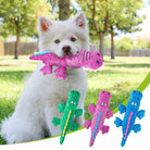 Weißer Hund im Park mit rosa Dinosaurier-Plüschtier im Maul. Hundespielzeug, Plüschdinosaurier, Haustierbedarf, Outdoor-Spielzeug.