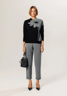 Damenmode: Eleganter schwarzer Pullover mit grauem Blumenmuster, kombiniert mit grauer Hose. Perfekt für stilvolle Herbst- und Winteroutfits.