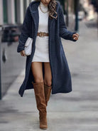 Frau in elegantem, blauem Teddy-Mantel, weißem Kleid und braunen Stiefeln. Modetrend Herbst/Winter, stilvoller Streetstyle-Look.