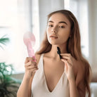 Frau mit rosa Handventilator und Schminkpinsel, modernes Interieur, natürliche Beleuchtung.