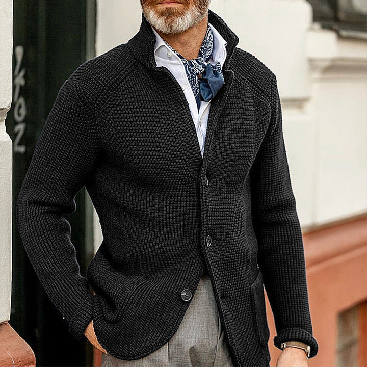 Eleganter Herren-Cardigan in Schwarz, kombiniert mit weißem Hemd und blauem Halstuch. Perfekt für stilvolle Herbst- und Wintermode.