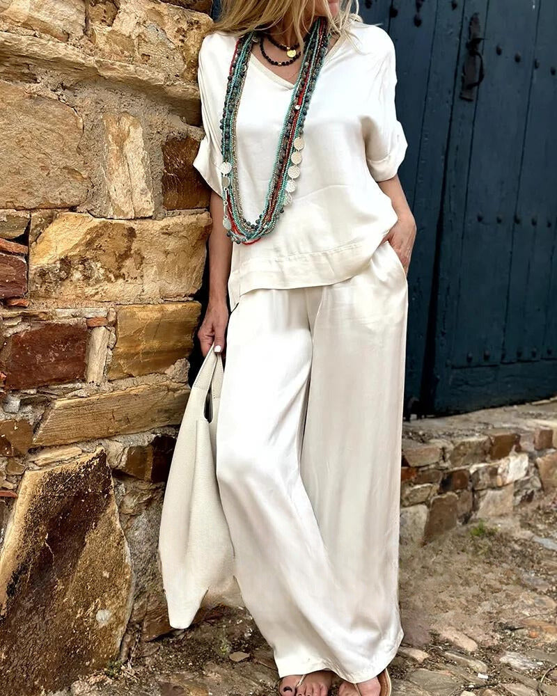 Elegantes Damen-Outfit in Weiß, bestehend aus lockerem Oberteil und Hose, ergänzt durch lange Halsketten. Perfekt für Sommermode und Freizeitlook.