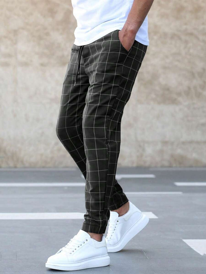 Mann trägt karierte Jogginghose in Dunkelgrün mit weißen Sneakern, lässiger Stil.