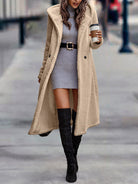 Damenmode: Langer, beiger Teddy-Mantel über grauem Strickkleid, kombiniert mit schwarzem Gürtel und Stiefeln. Trendiger Herbst-Look.