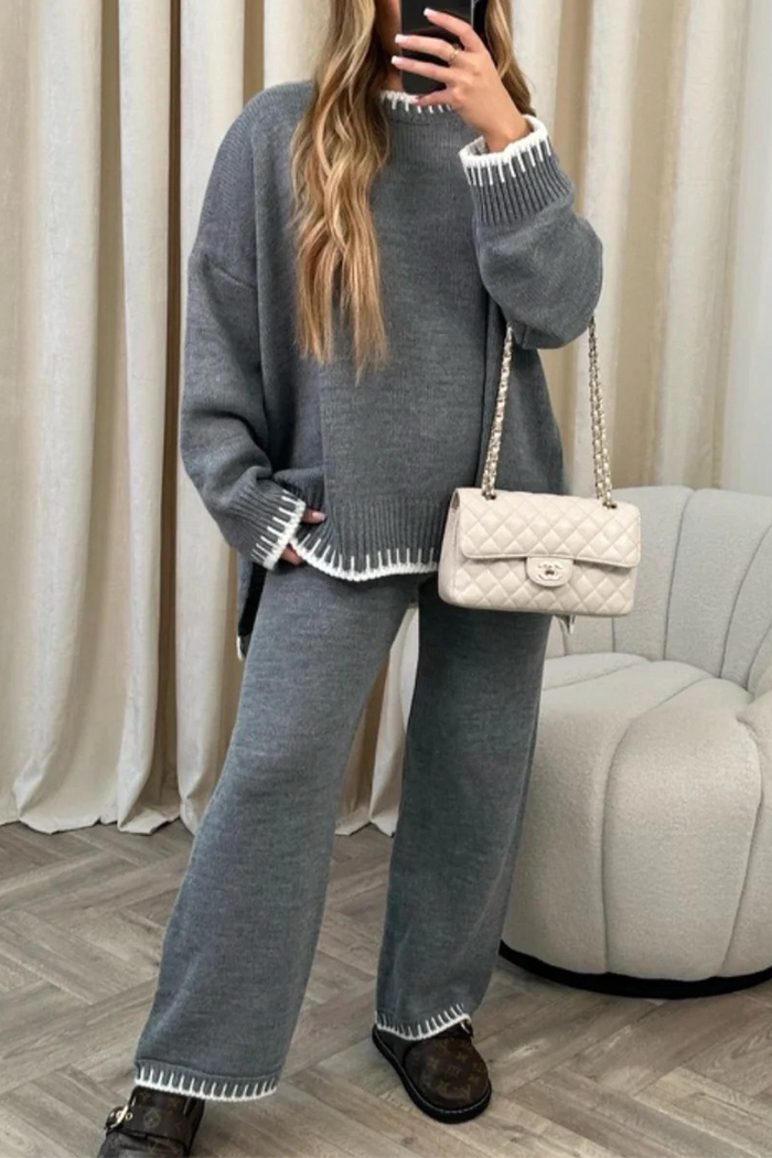 Frau in grauem Strick-Set mit weißem Rand, hält eine gesteppte Handtasche. Modetrend, gemütlicher Look, Herbstmode, Damenbekleidung.