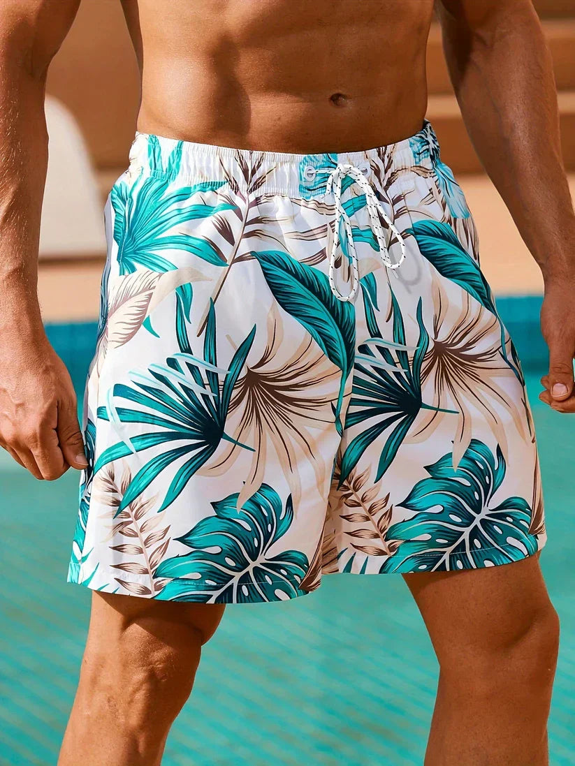 Herren-Badeshorts mit tropischem Blattmuster, weiß und türkis, ideal für Sommer und Strand.