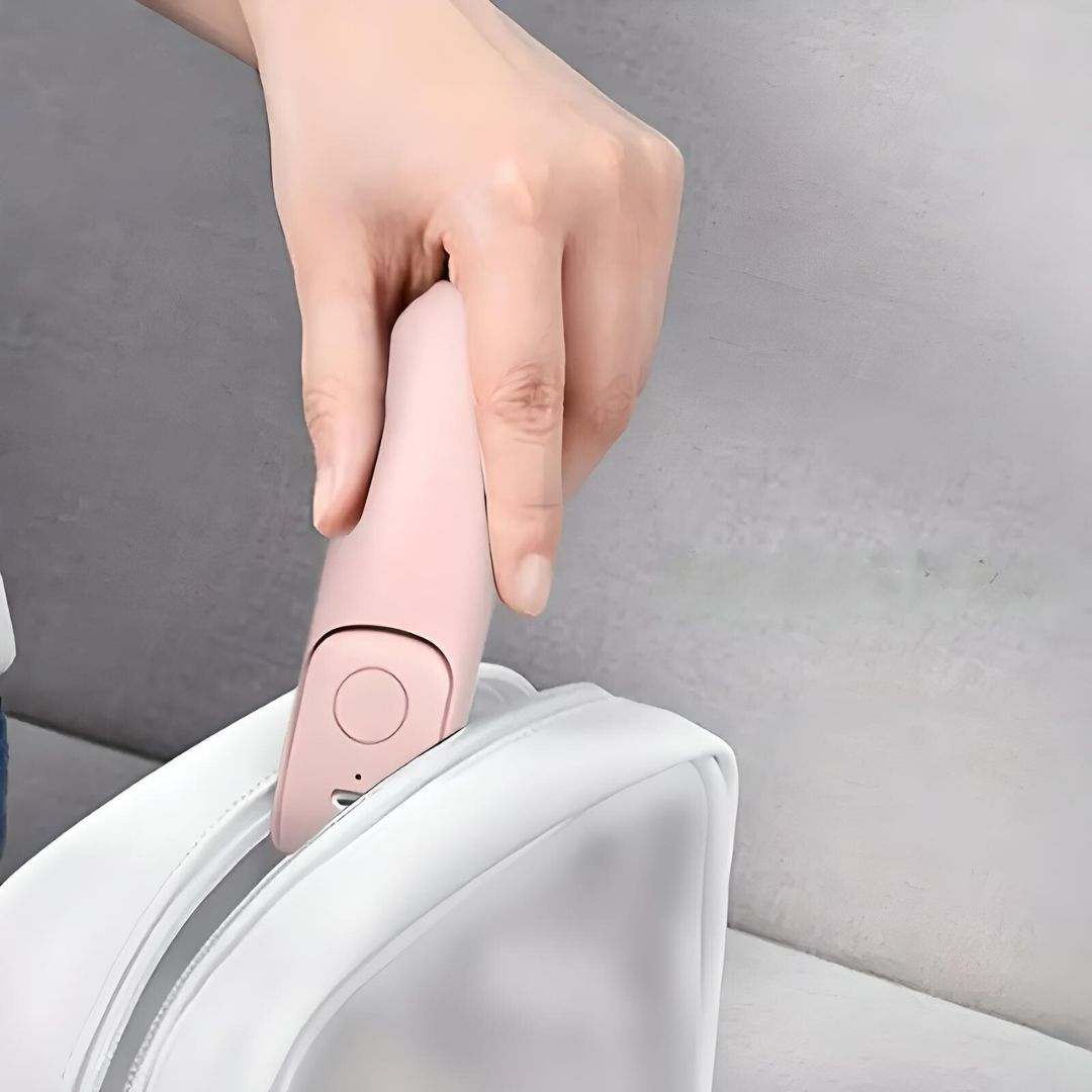 Hand hält rosa Mini-Bügeleisen, tragbar, in weißer Tasche, Reisebügeleisen, kompakt.