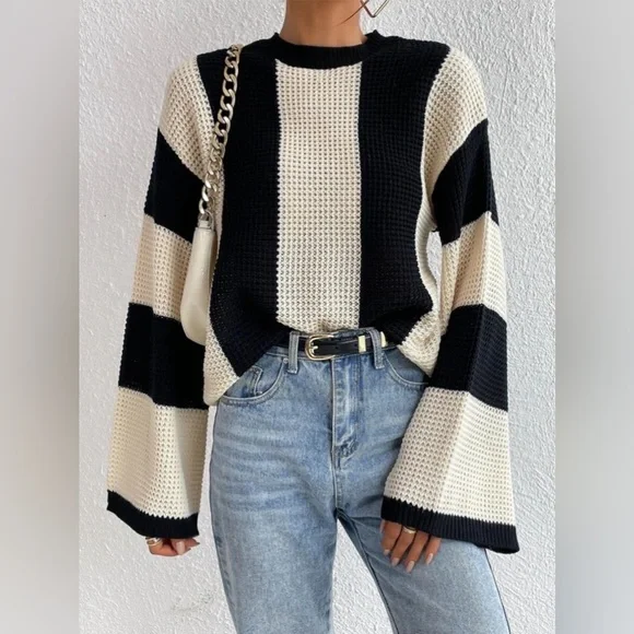 Gestreifter Pullover in Schwarz-Weiß mit weitem Schnitt, kombiniert mit blauer Jeans und weißer Handtasche. Modetrend, lässiger Look, Damenmode.