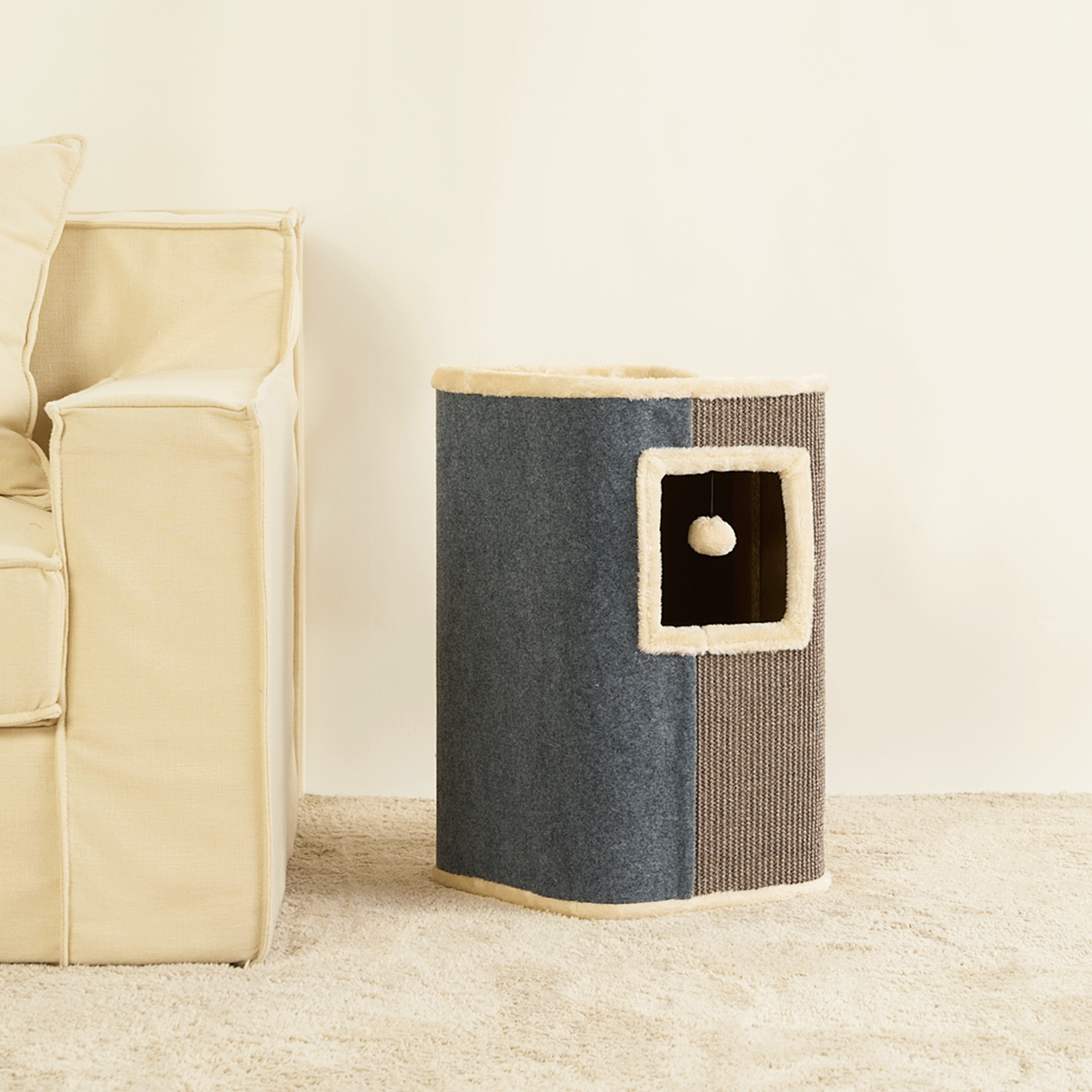 Katzenhaus aus Stoff und Sisal, blau und beige, mit Spielzeug, neben beigem Sofa auf Teppich.