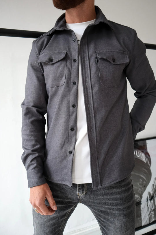 Graues Herrenhemd mit Knopfleiste und Brusttaschen, kombiniert mit weißem T-Shirt und Jeans. Stilvolle Herrenmode, lässiger Look.