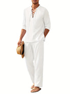 Mann in weißem Leinenanzug mit Schnürhemd, hält Strohhut, trägt Sandalen. Sommermode, lässiger Strandlook, Herrenbekleidung, stilvoll.