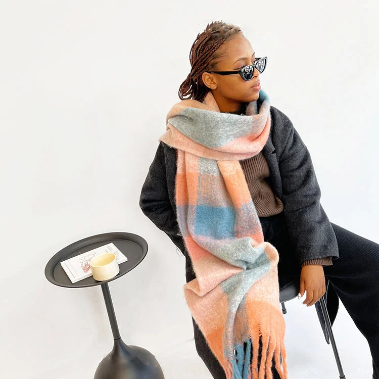 Frau mit kariertem Schal in Pastellfarben, sitzt stilvoll auf einem Stuhl. Modetrend, Winteraccessoire, Damenmode, eleganter Look.