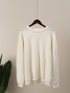 Weißer Strickpullover auf Holzkleiderbügel, minimalistisch, gemütlich, ideal für Herbstmode. Hochwertige Baumwolle, lässiger Stil, unisex.
