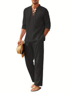 Mann in schwarzem Leinenhemd mit Schnürung, hält Strohhut, trägt Flip-Flops. Sommermode, Herrenbekleidung, lässiger Stil, Strandoutfit.