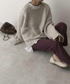 Gemütlicher, beiger Strickpullover mit Tasche, kombiniert mit lila Hose und beigen Schuhen. Perfekt für lässige Herbstmode und Streetstyle.