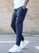 Mann in karierten blauen Jogginghosen und weißen Sneakers auf grauem Hintergrund.