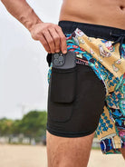 Mann in bunter Badeshorts mit Smartphone in der Tasche am Strand.