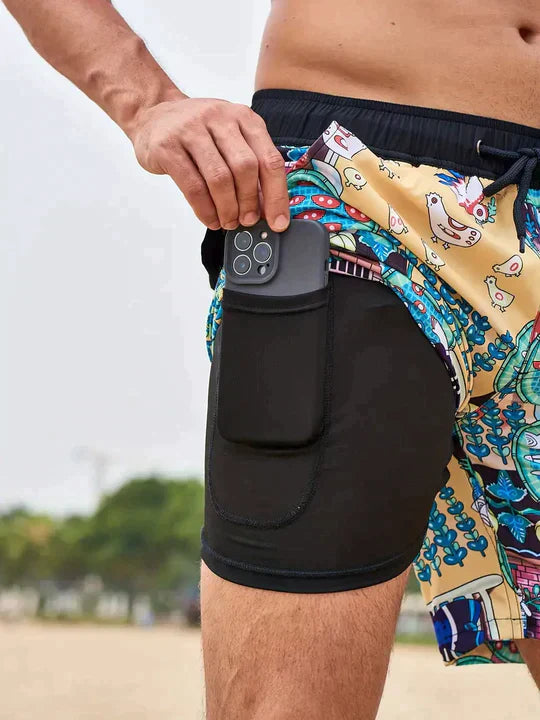 Mann in bunter Badeshorts mit Smartphone in der Tasche am Strand.