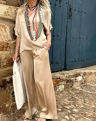 Frau in eleganter, beiger Seidenhose und Bluse, trägt lange Halsketten. Perfekt für Sommermode, Boho-Stil, lässige Eleganz.