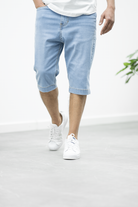 Mann trägt blaue Jeans-Bermudashorts, lässiger Stil, weiße Sneaker, Sommermode.