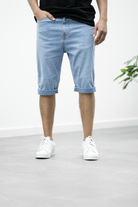 Mann in hellblauen Jeans-Bermudashorts, lässiger Stil, weiße Sneaker, moderne Herrenmode.
