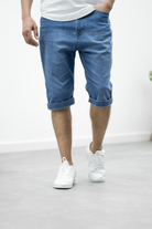 Mann trägt blaue Jeans-Bermudashorts, lässiger Stil, weiße Sneaker, modische Herrenbekleidung.